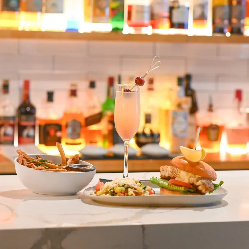 French fries, a fish sandwich, salad, and pink cocktail on a marble bar.