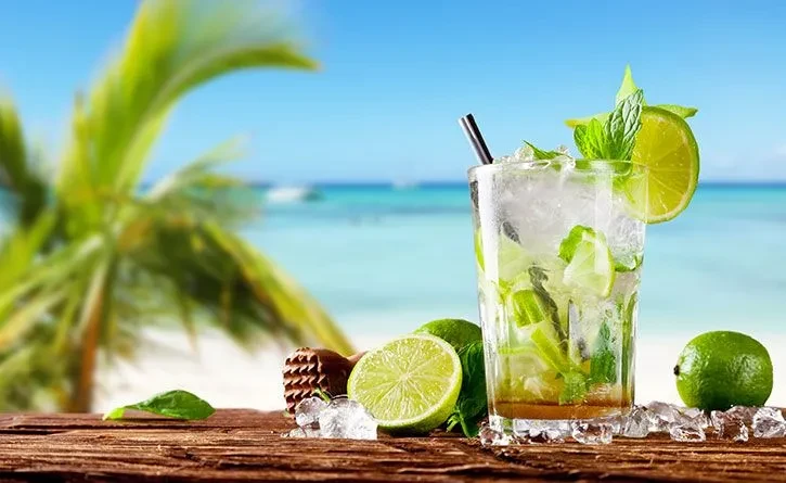 Mojito with lime and mint on wood, blurred tropical beach background.