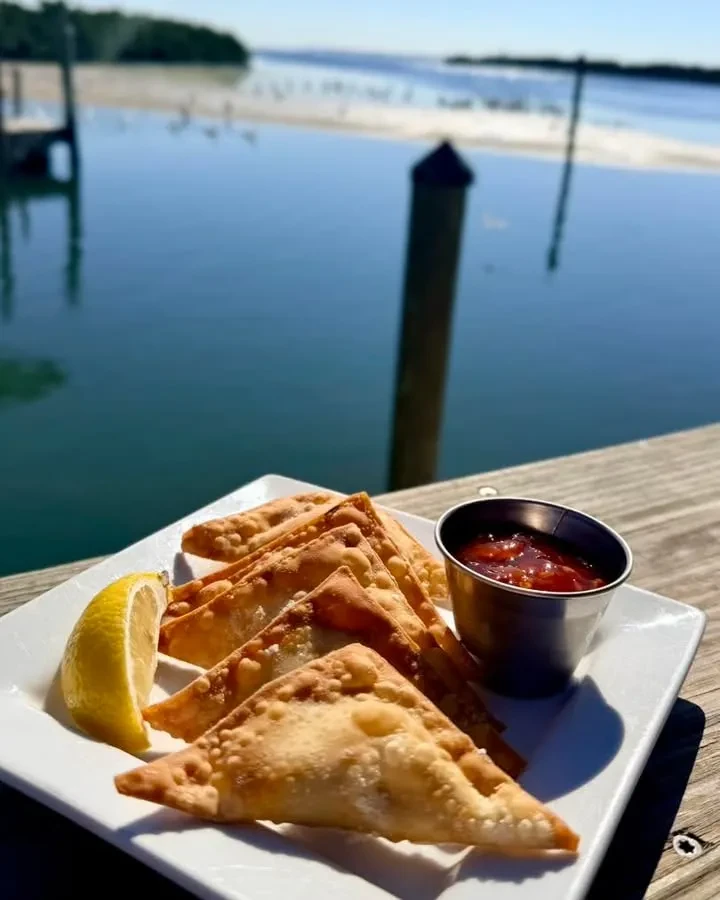 Fried triangle pastries, lemon, sauce, overlooking water.