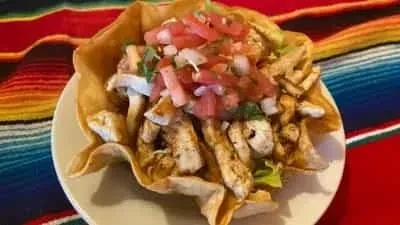 Chicken taco salad in a crispy bowl with a vibrant striped background.