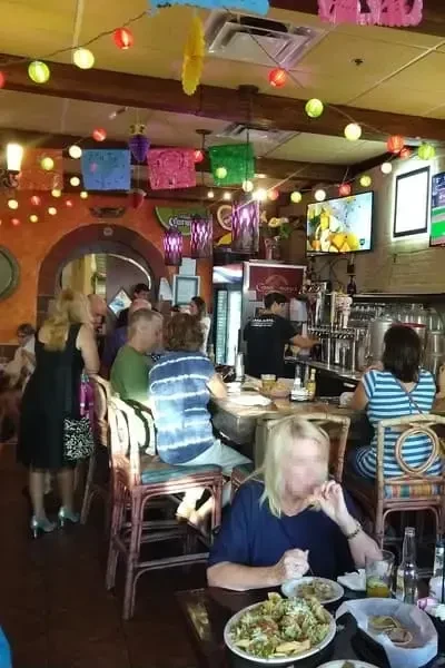 Bustling restaurant with patrons at a bar and festive decor.