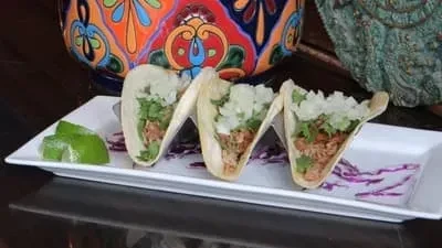 Three street tacos with shredded meat, onion, cilantro, lime, and cabbage.