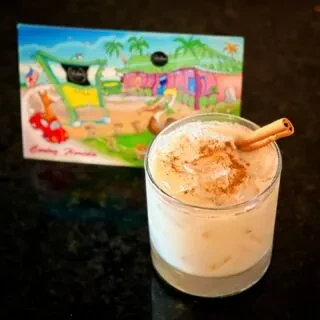 A creamy, iced drink with cinnamon next to a tropical beach box.