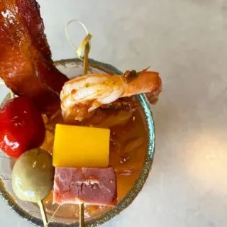 Overhead view of an elaborately garnished savory cocktail with bacon and shrimp.