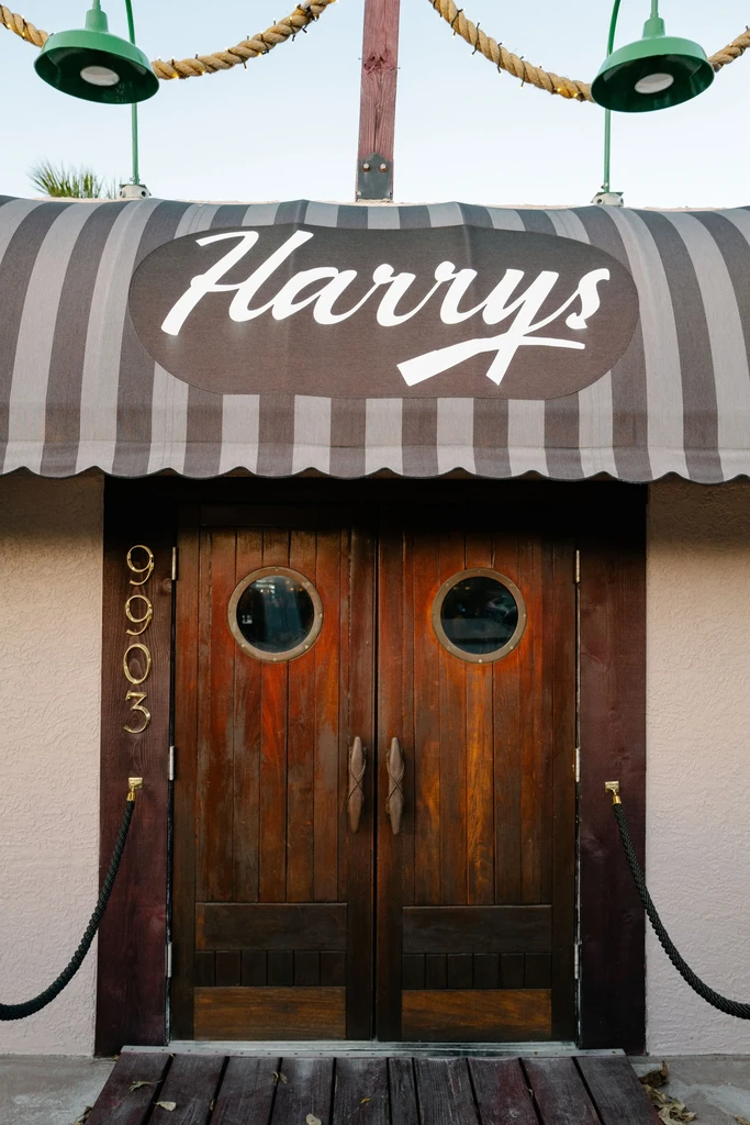 Harry's restaurant entrance with porthole doors, striped awning, and lamps.