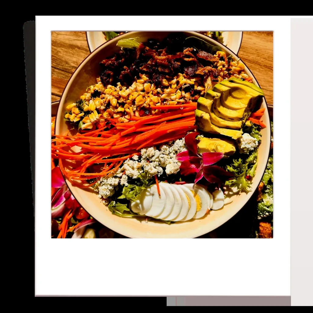 Colorful salad with bacon, corn, carrots, egg, avocado, and an orchid.