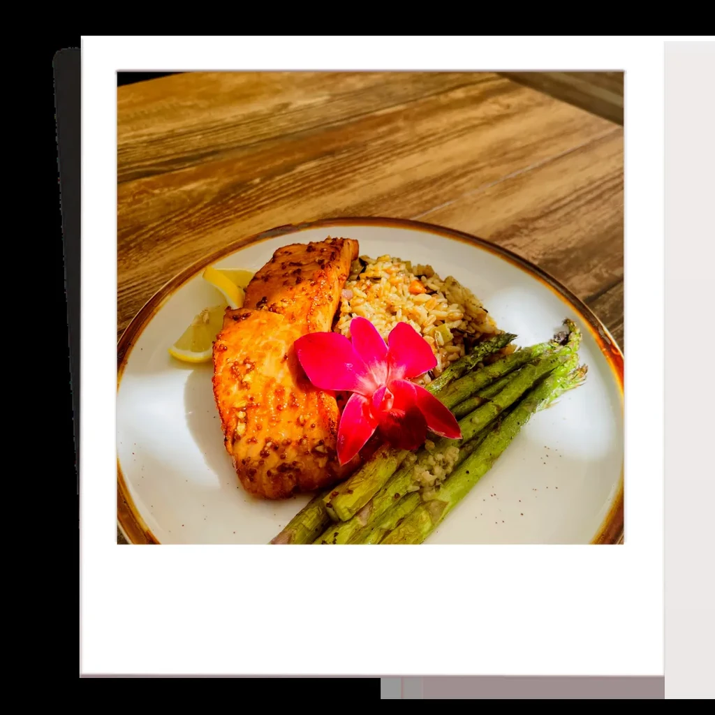Plated seared salmon with asparagus, rice, pink orchid, and lemon.
