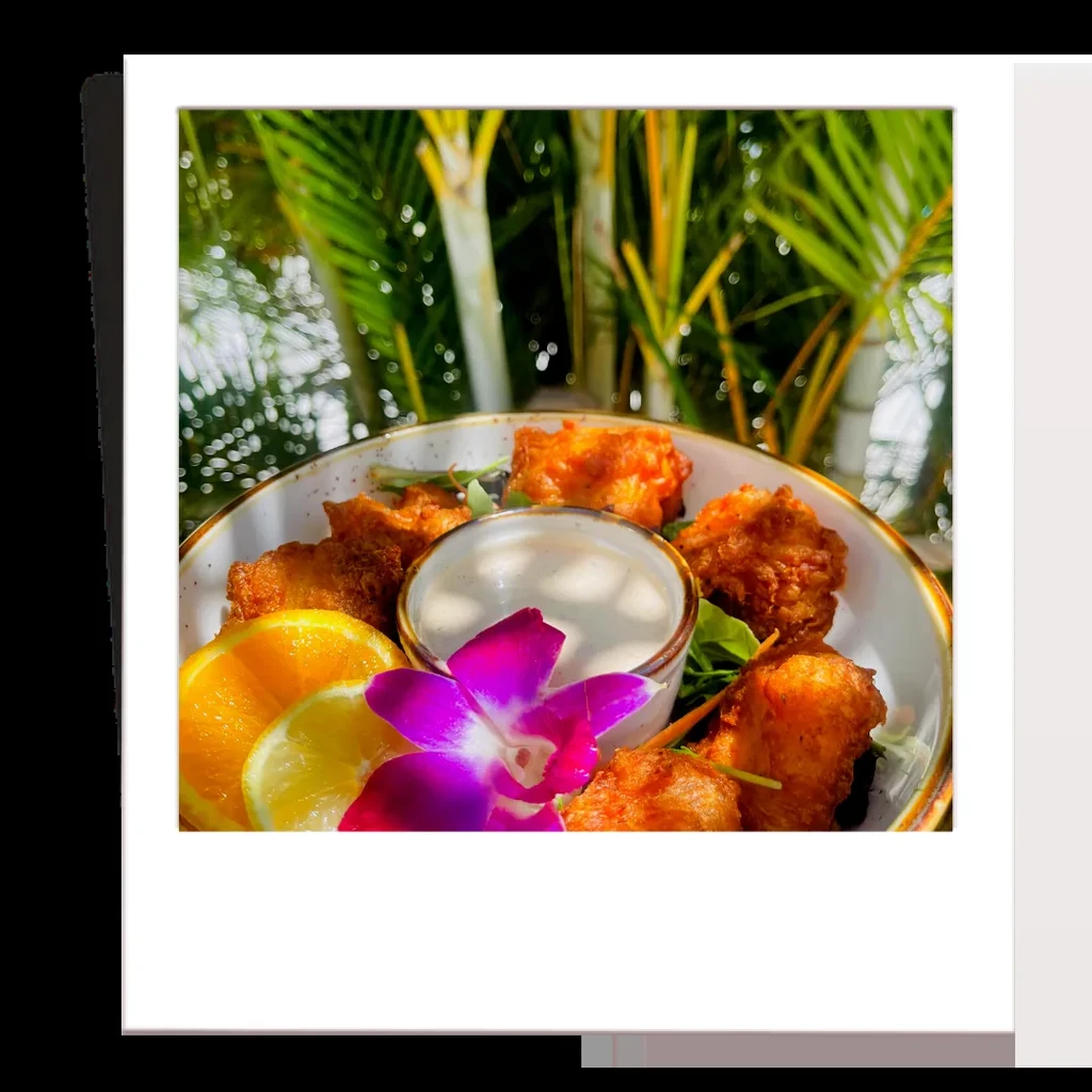 Crispy golden fritters with sauce, citrus, orchid, and tropical background.