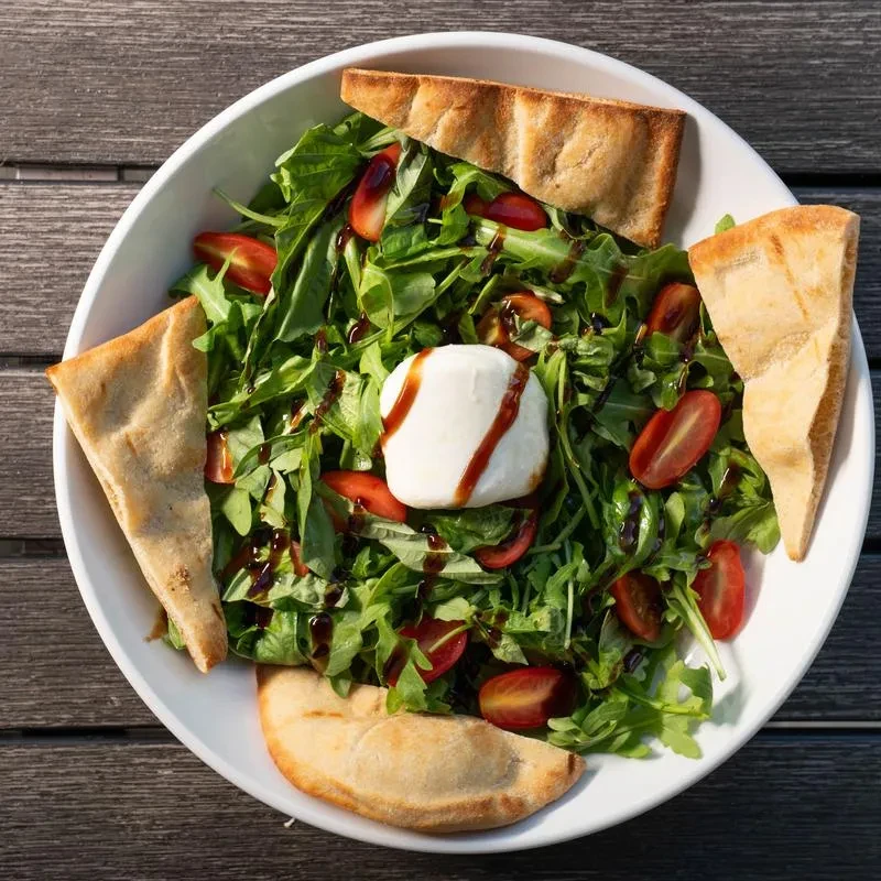 Salad with greens, tomatoes, mozzarella, balsamic, flatbread on a wooden table.