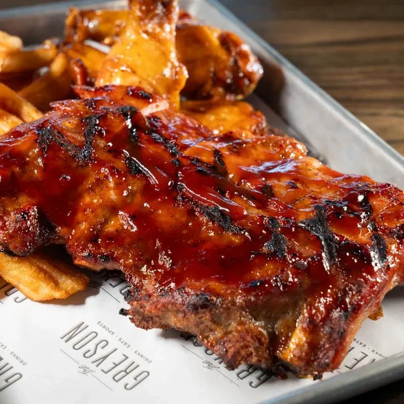 Close-up of BBQ ribs, chicken wings, and fries on a branded tray.