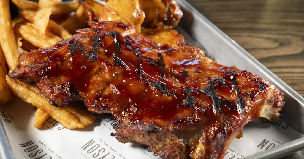 Barbecued ribs and crinkle-cut fries served on a metal tray.