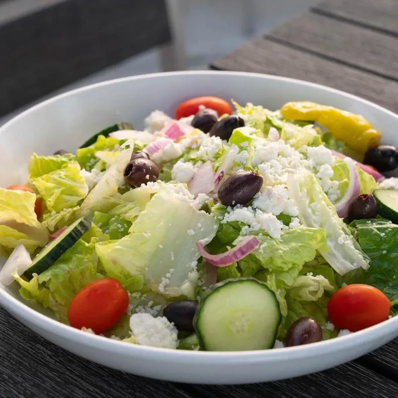 Vibrant Greek salad in a white bowl with olives, feta, and pepperoncini.