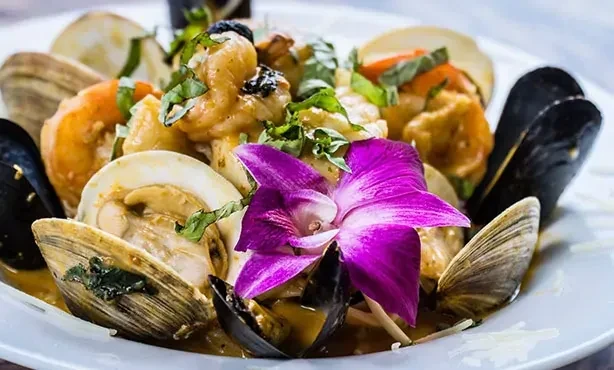 Close-up of seafood dish with clams, mussels, shrimp, herbs, and orchid.