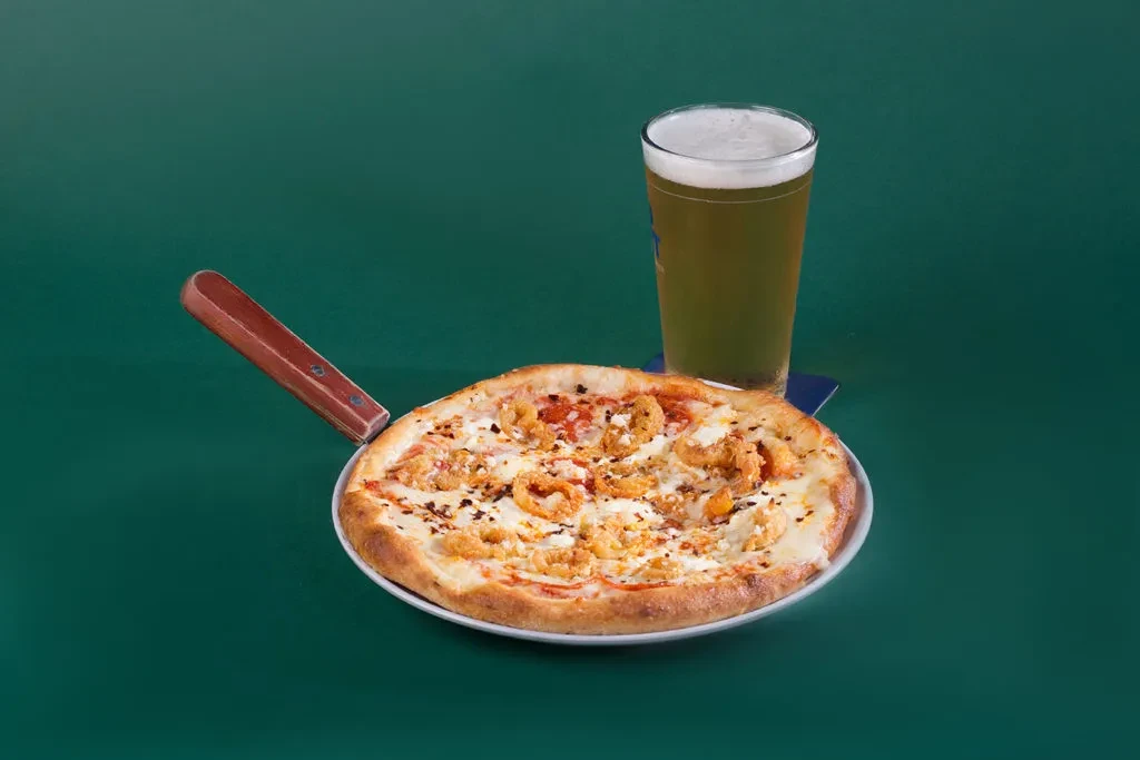 Seafood pizza on a wooden peel, beside a glass of beer.