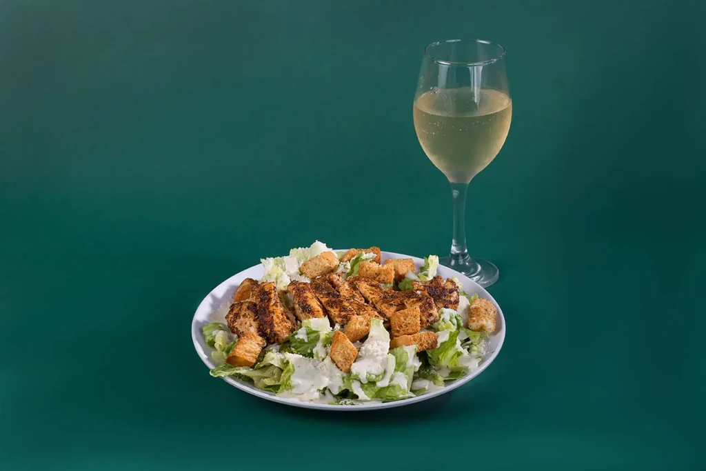 Grilled chicken Caesar salad with croutons and a glass of wine.