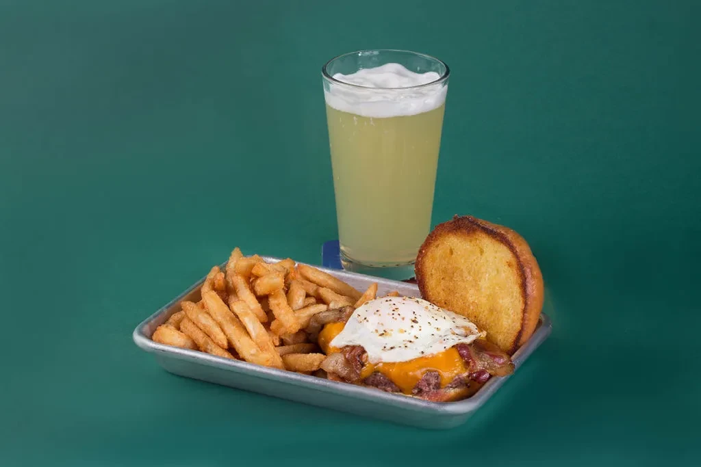 Loaded burger with fried egg, golden fries, and a foamy drink.