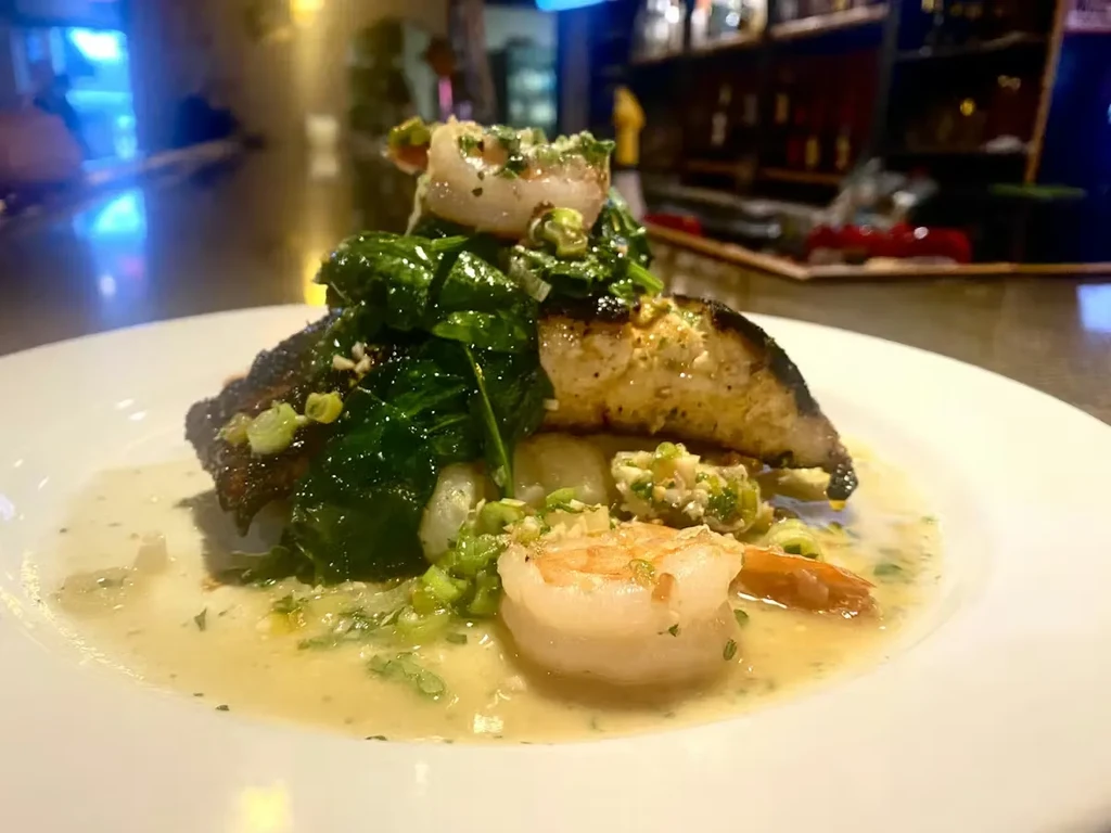 Plated fish with shrimp, leafy greens, and light herb sauce.