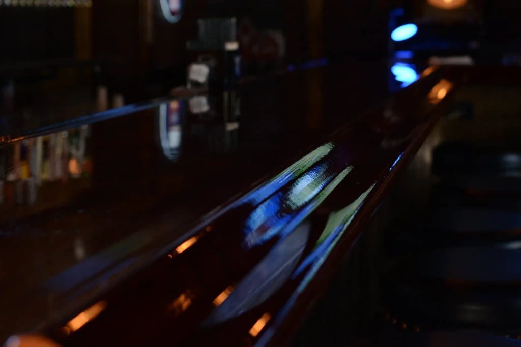 Dark, reflective reddish-brown bar top reflecting blurred colorful light streaks.