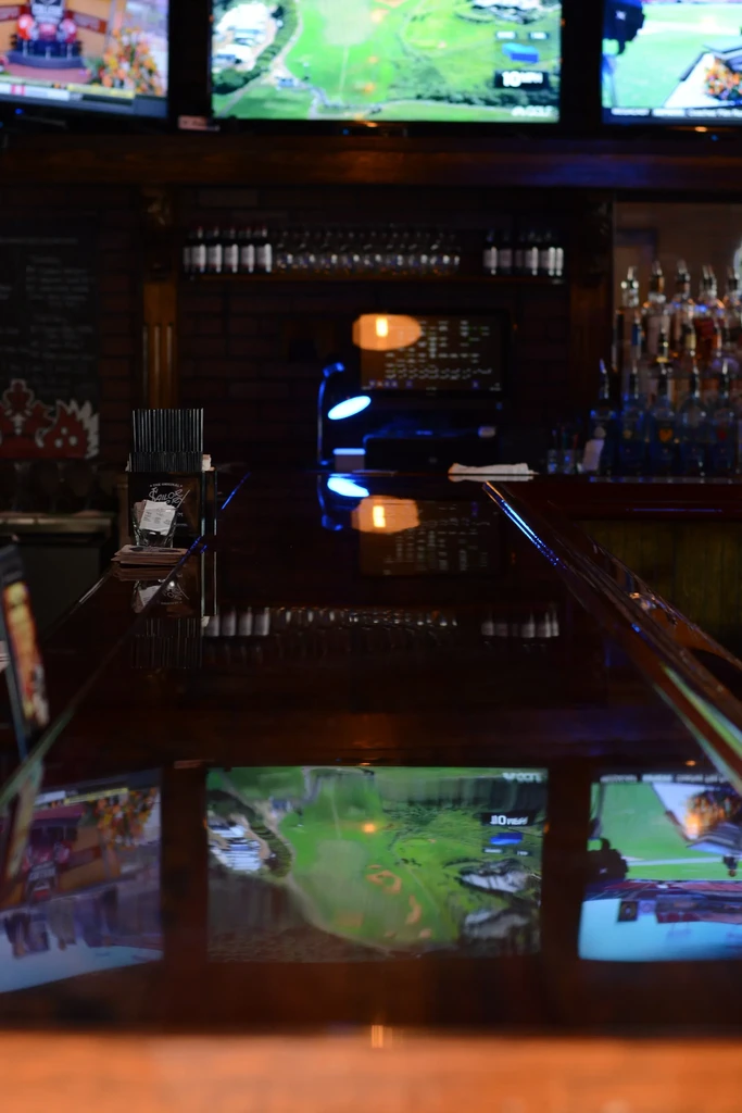 Dimly lit bar interior showing TVs, golf course reflected on counter.