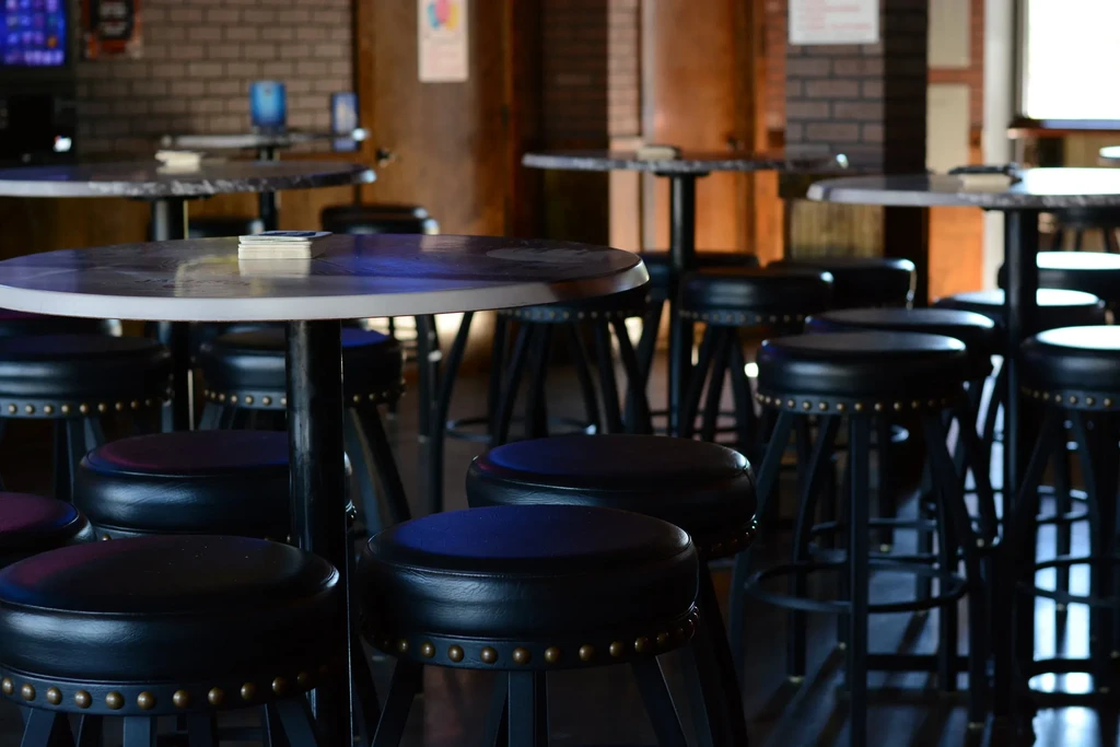 Dim bar interior with high-top tables, studded stools, and brick wall.