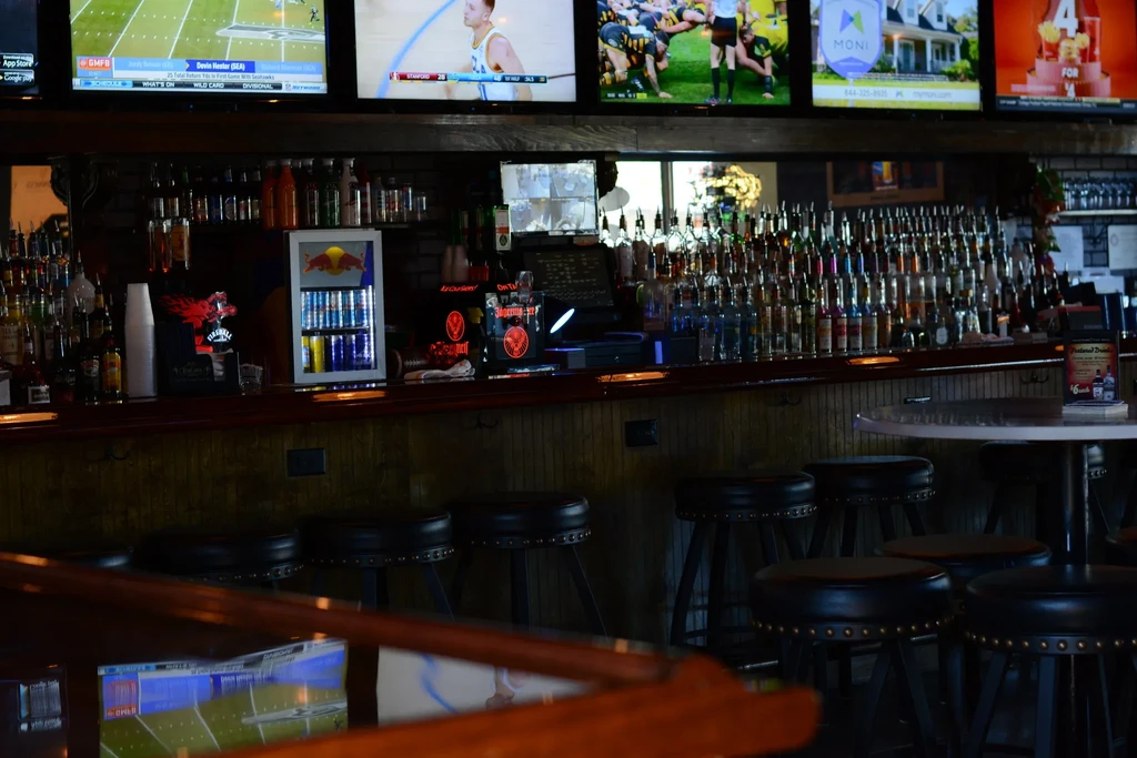 Dim sports bar interior with liquor display and multiple TVs showing sports.