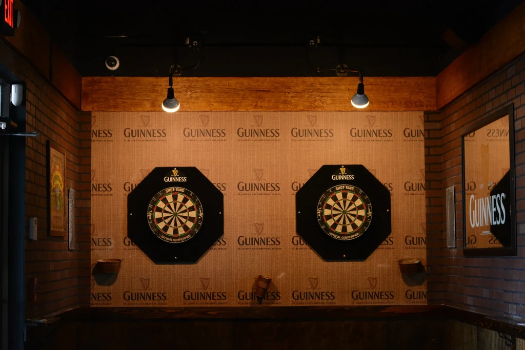 Two octagonal dartboards on a Guinness-branded wall in a pub.