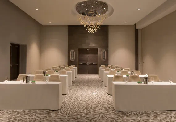 Symmetrical, empty banquet room with set tables, chairs, and chandelier.