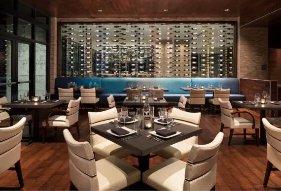 Upscale restaurant dining area featuring tables, banquettes, and a large wine wall.