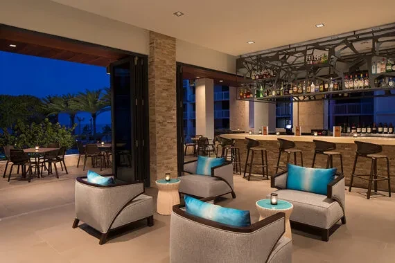 Modern bar and lounge opens to a lit tropical patio at dusk.