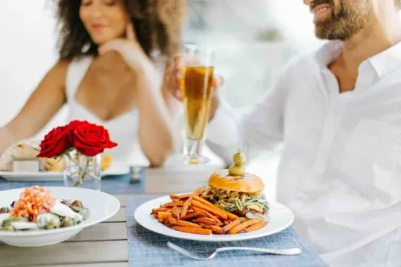 Two people dining with a burger, fries, seafood, and drinks.