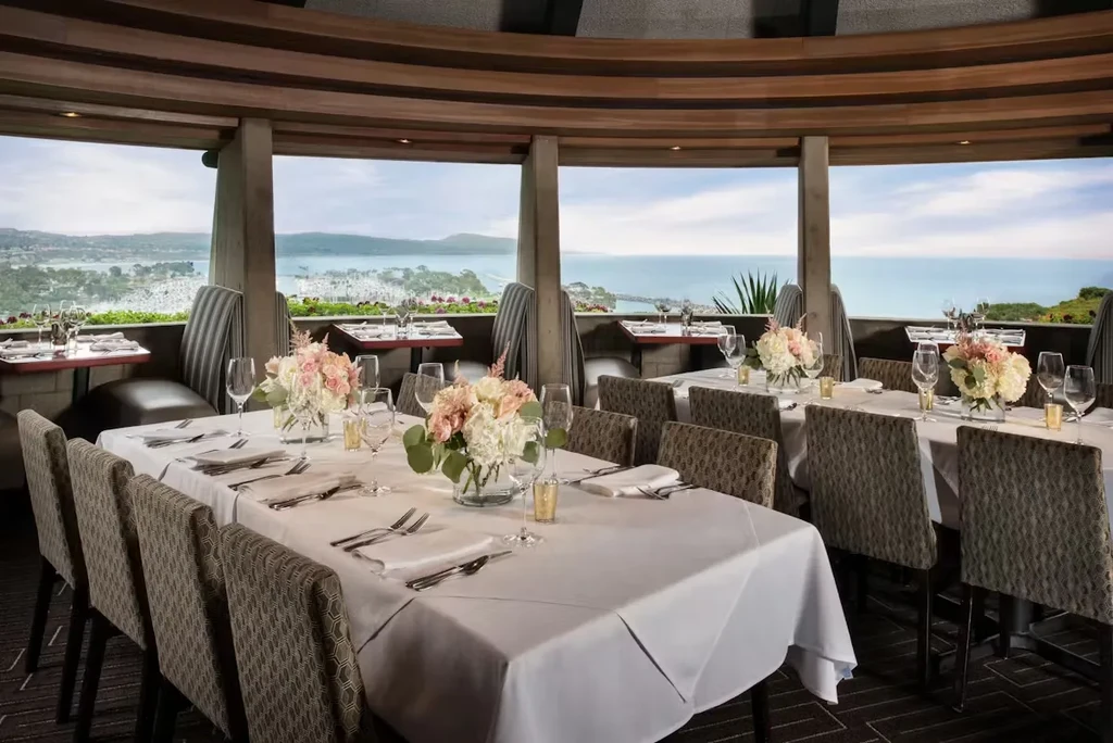 Upscale restaurant dining room with set tables and panoramic ocean view.