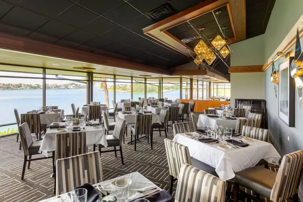Upscale restaurant dining room with set tables and panoramic water view.
