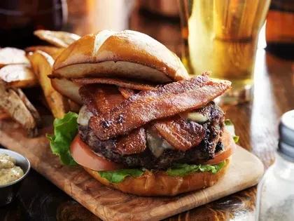 Gourmet bacon cheeseburger on pretzel bun with steak fries.
