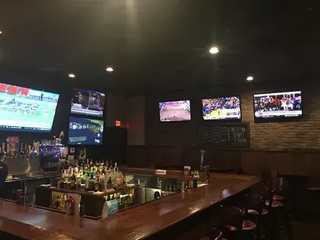 Dimly lit sports bar interior with long wooden bar and multiple TVs.