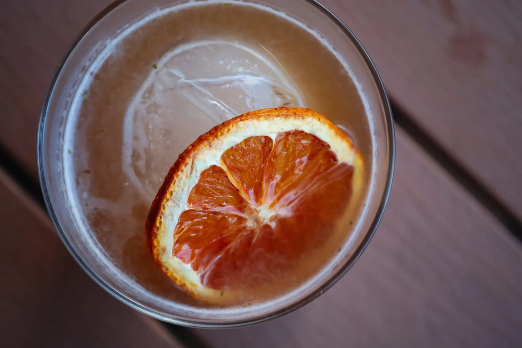 Top-down view: Amber drink, round ice, dried blood orange.