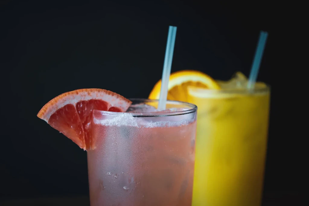 Two frosted, iced drinks with fruit slices against a dark background.