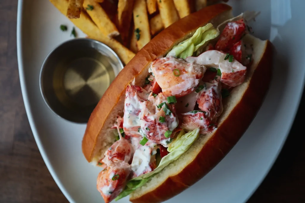 Lobster roll with creamy filling, fries, and melted butter.