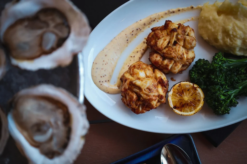 Plated crab cakes, creamy sauce, broccoli, mashed potatoes, grilled lemon.