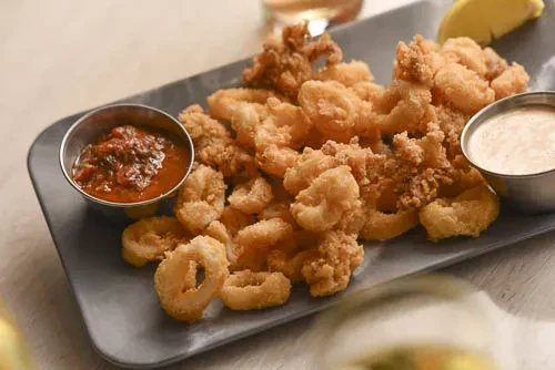 Plate of crispy fried calamari with two dipping sauces and lemon.