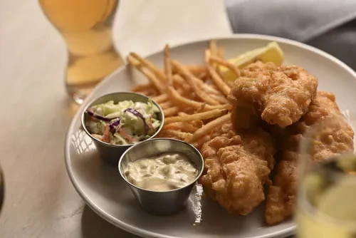 Plate of fish and chips with coleslaw, tartar sauce, and lemon.