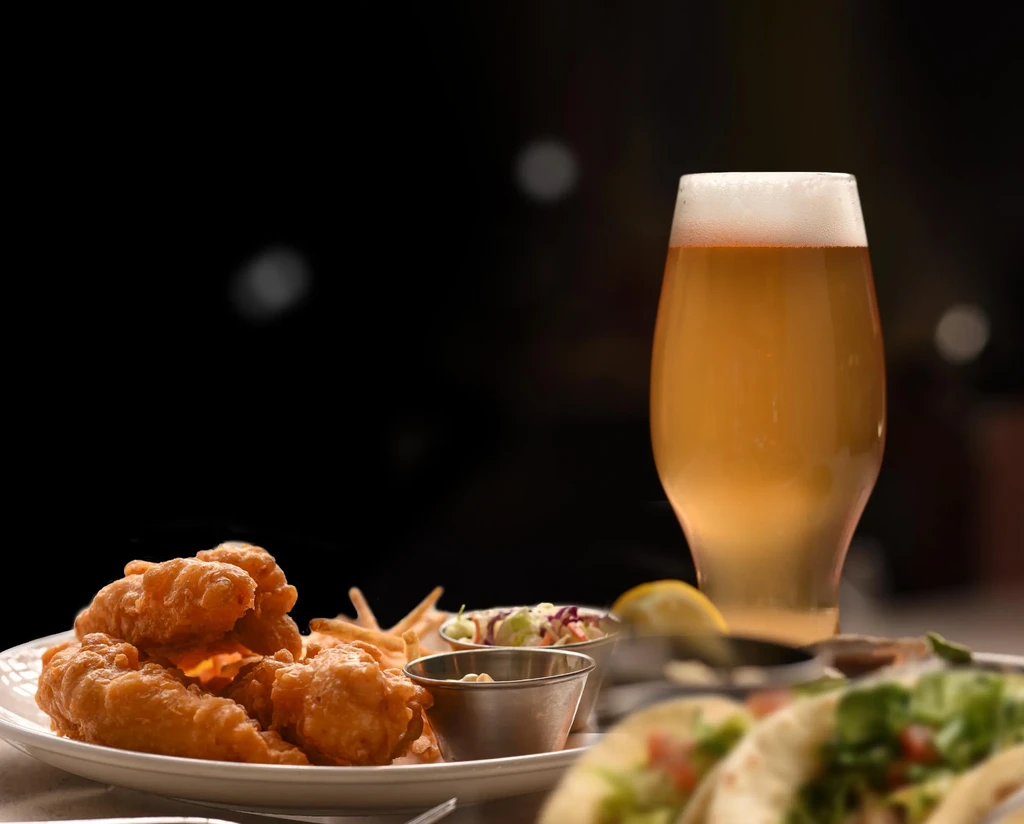 Fried food, waffle fries, beer, and tacos on a restaurant table.