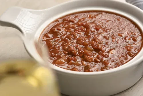 Glossy, chunky red stew with meat and beans in a white bowl.