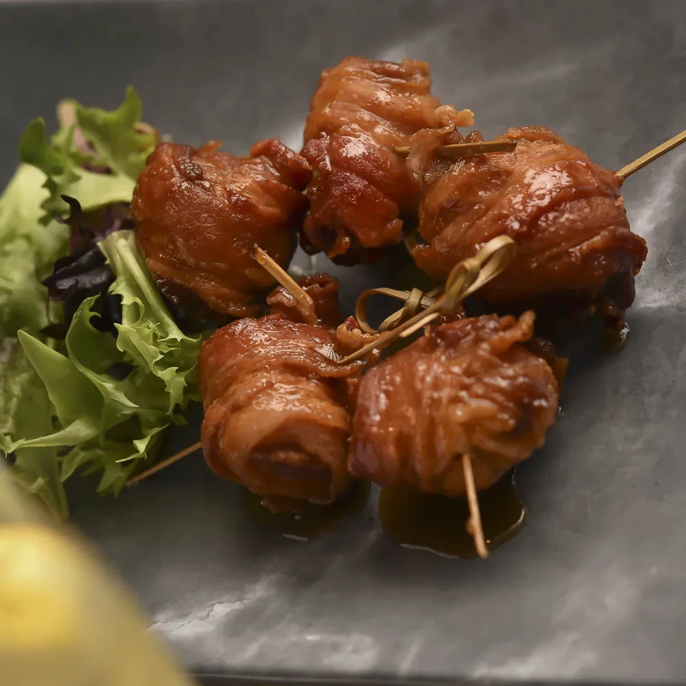 Glazed meat skewers with sauce and fresh greens on a dark grey plate.