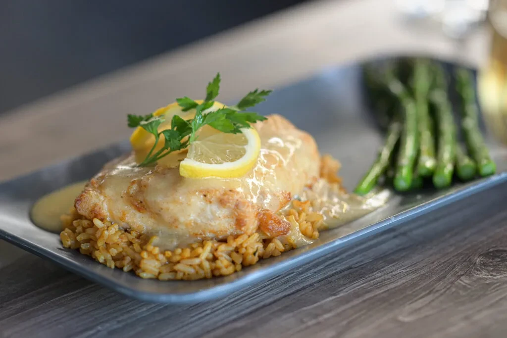 Chicken or fish with creamy sauce, rice, asparagus, and lemon.