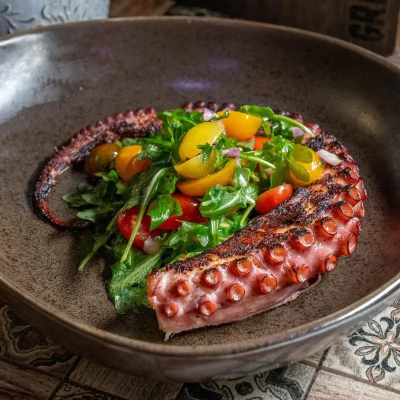 Charred grilled octopus tentacle with arugula and tomato salad.