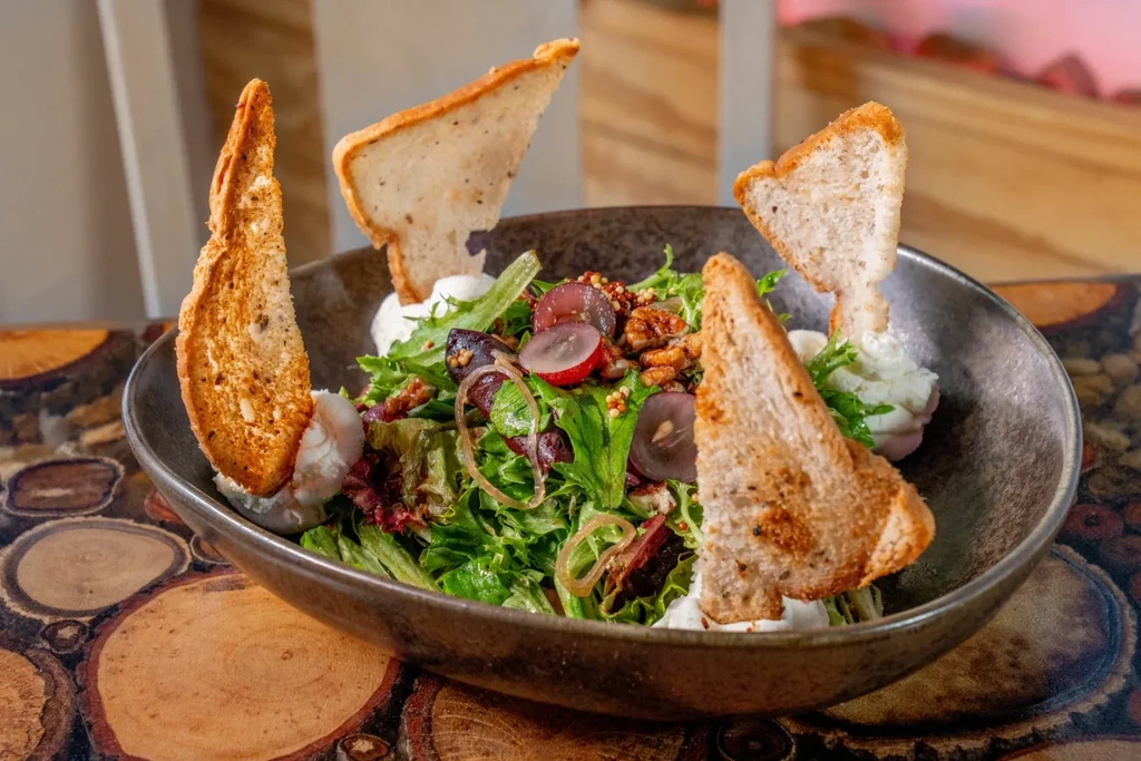 Fresh salad with grapes, walnuts, cheese, and bread, on a polished wood table.