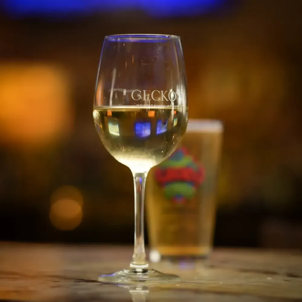 White wine glass with GECKO HOSPITALITY GROUP logo, colorful reflections.