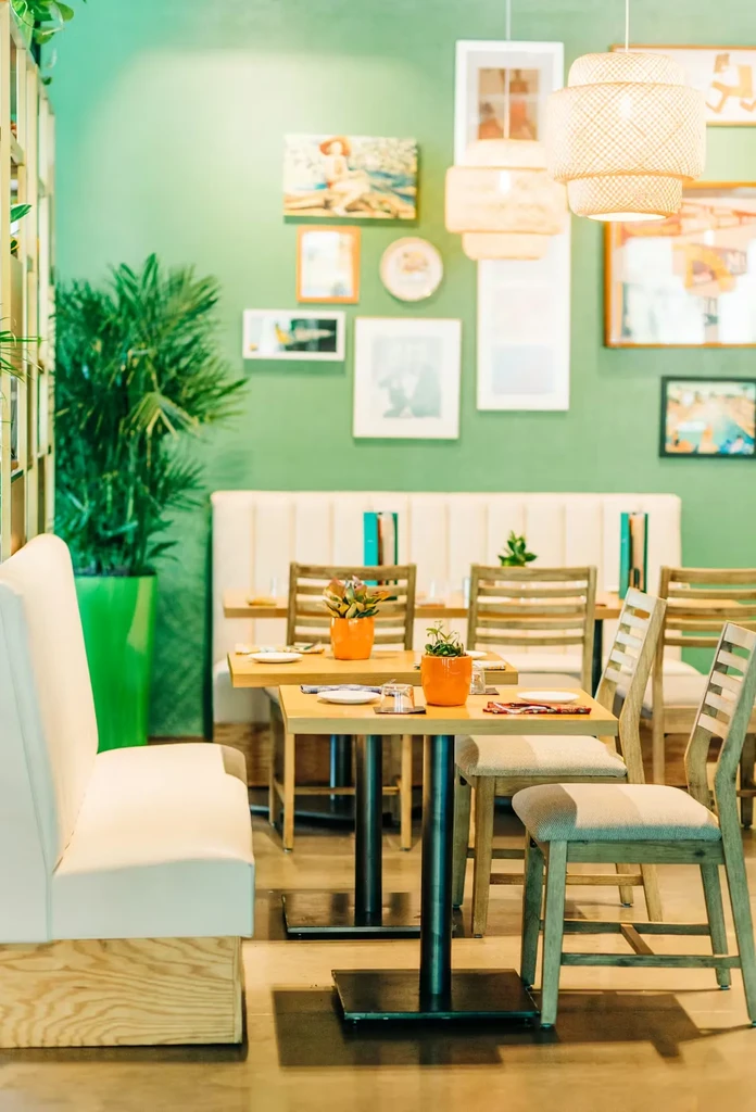 Bright restaurant dining area with green walls, set tables, and woven lights.