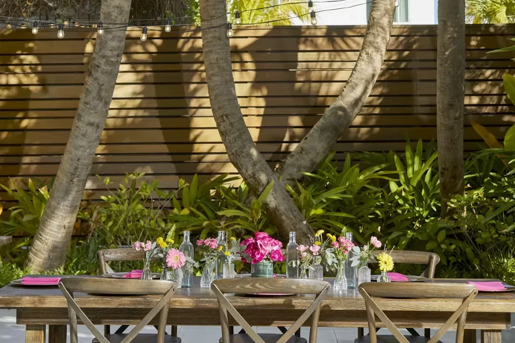 Outdoor dining table with colorful flowers, tropical foliage, and string lights.