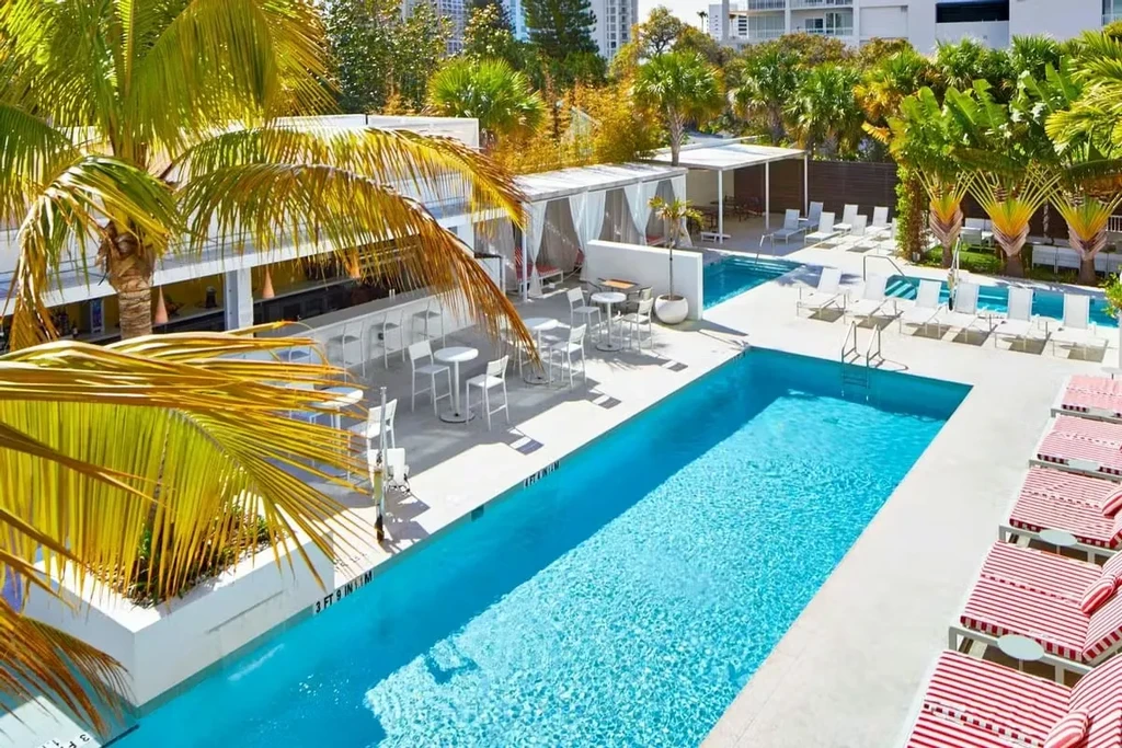 Elevated view of a sunlit tropical resort with two blue swimming pools.
